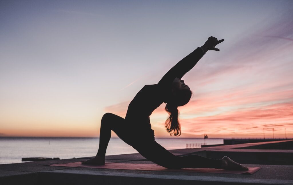 A woman practicing yoga on a beach at sunrise